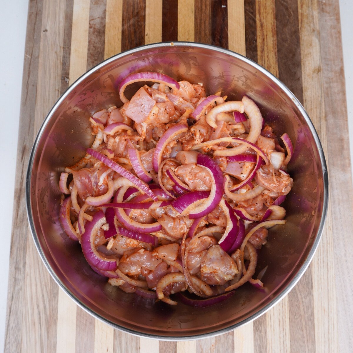 cubed chicken thighs with sliced onion and seasoning in a yeti mixing bowl.