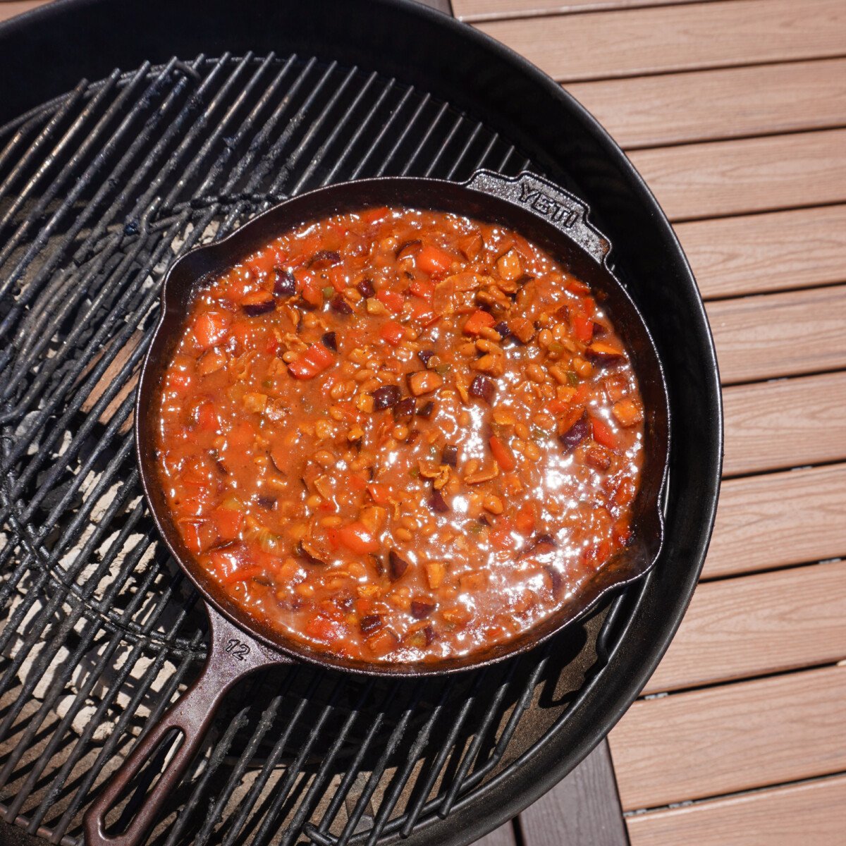 smoked pit beans in cast iron skillet on charcoal grill.