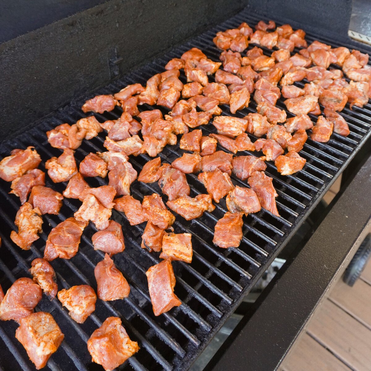 pork shoulder bites seasoned and on the smoker grates.