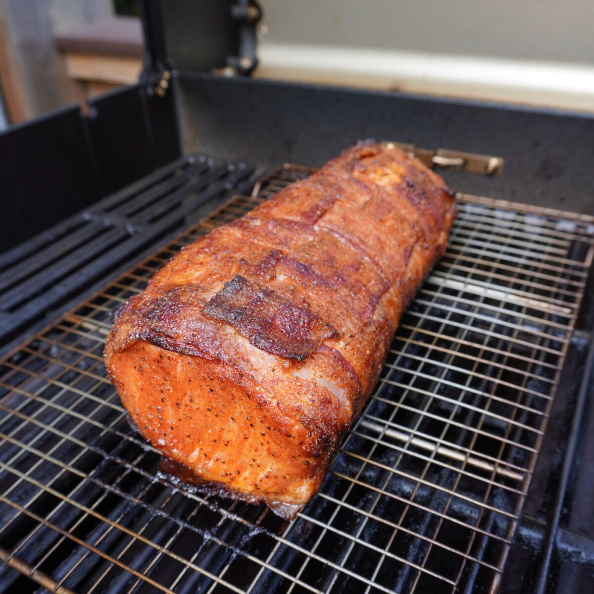 bacon wrapped pork loin on a wire rack on the grill.