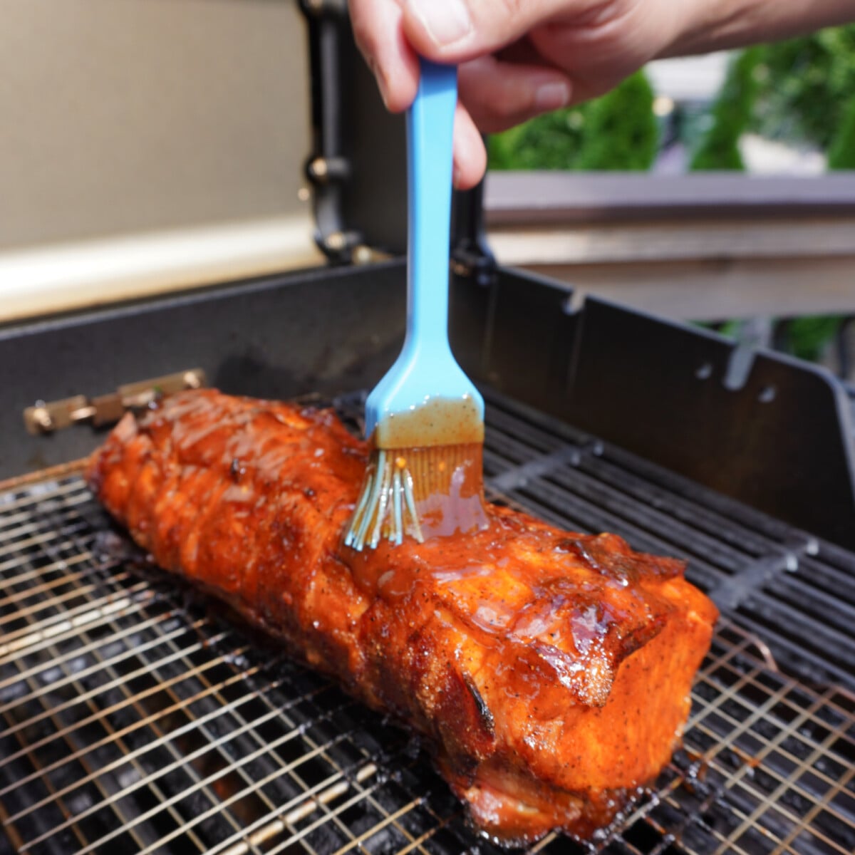 Brushing a bacon wrapped pork loin with BBQ sauce.