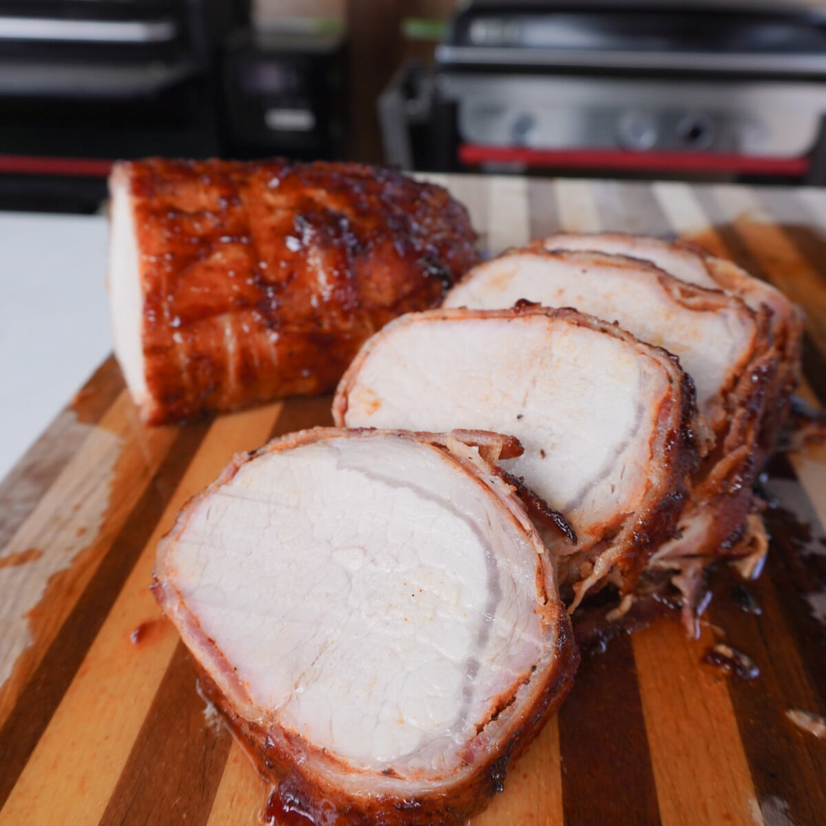 Grilled Bacon Wrapped Pork Loin sliced on a cutting board.