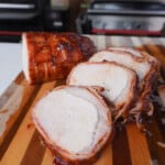 Grilled Bacon Wrapped Pork Loin sliced on a cutting board.