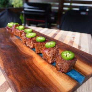 burnt ends in beer bbq sauce lined up on cutting board with jalapeno slices on top.