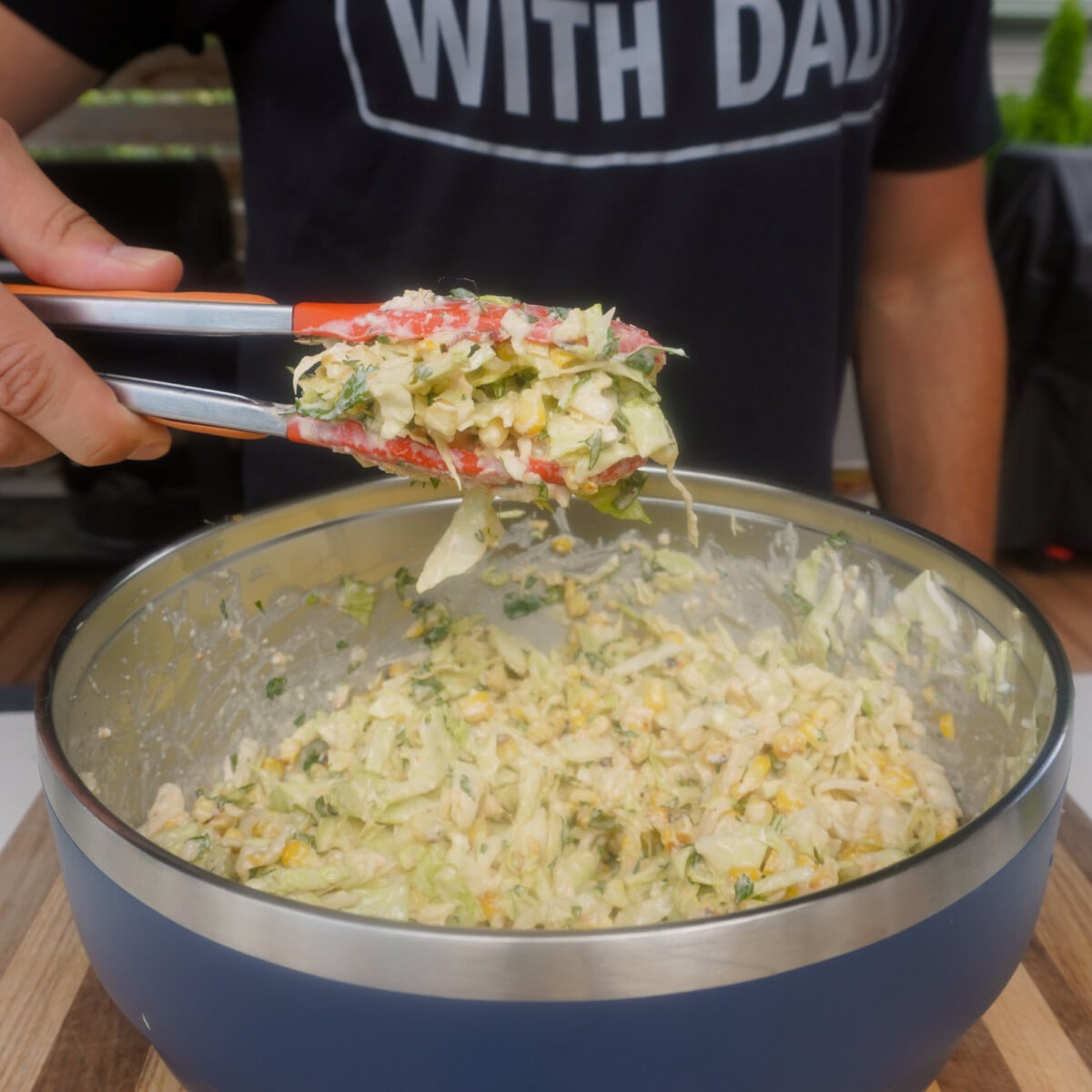 corn slaw mixed together in yeti bowl.  Tongs showcasing a batch above the bowl for the grilled shrimp with corn slaw tacos.