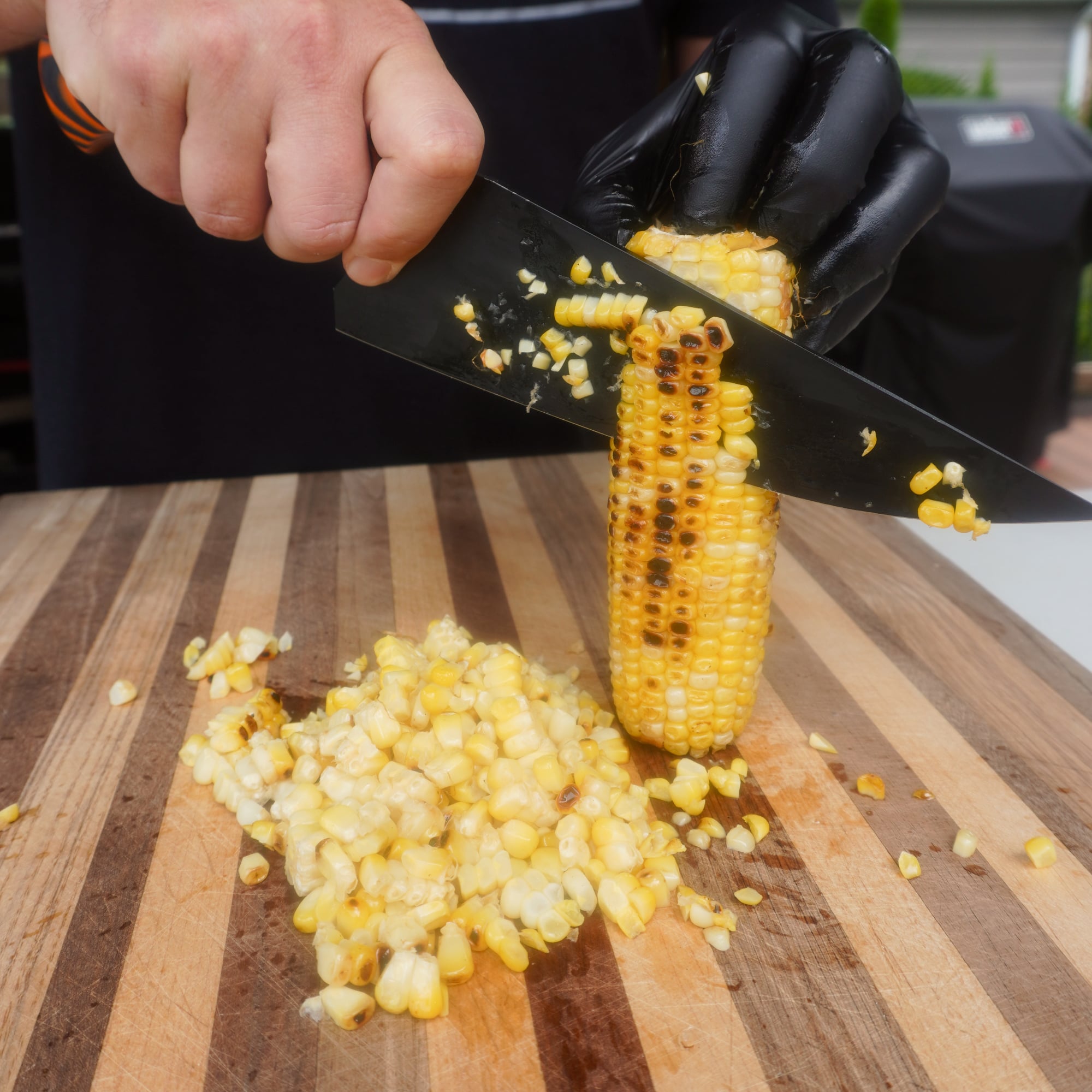 knife cutting off fire roasted kernels off corn on the cob.
