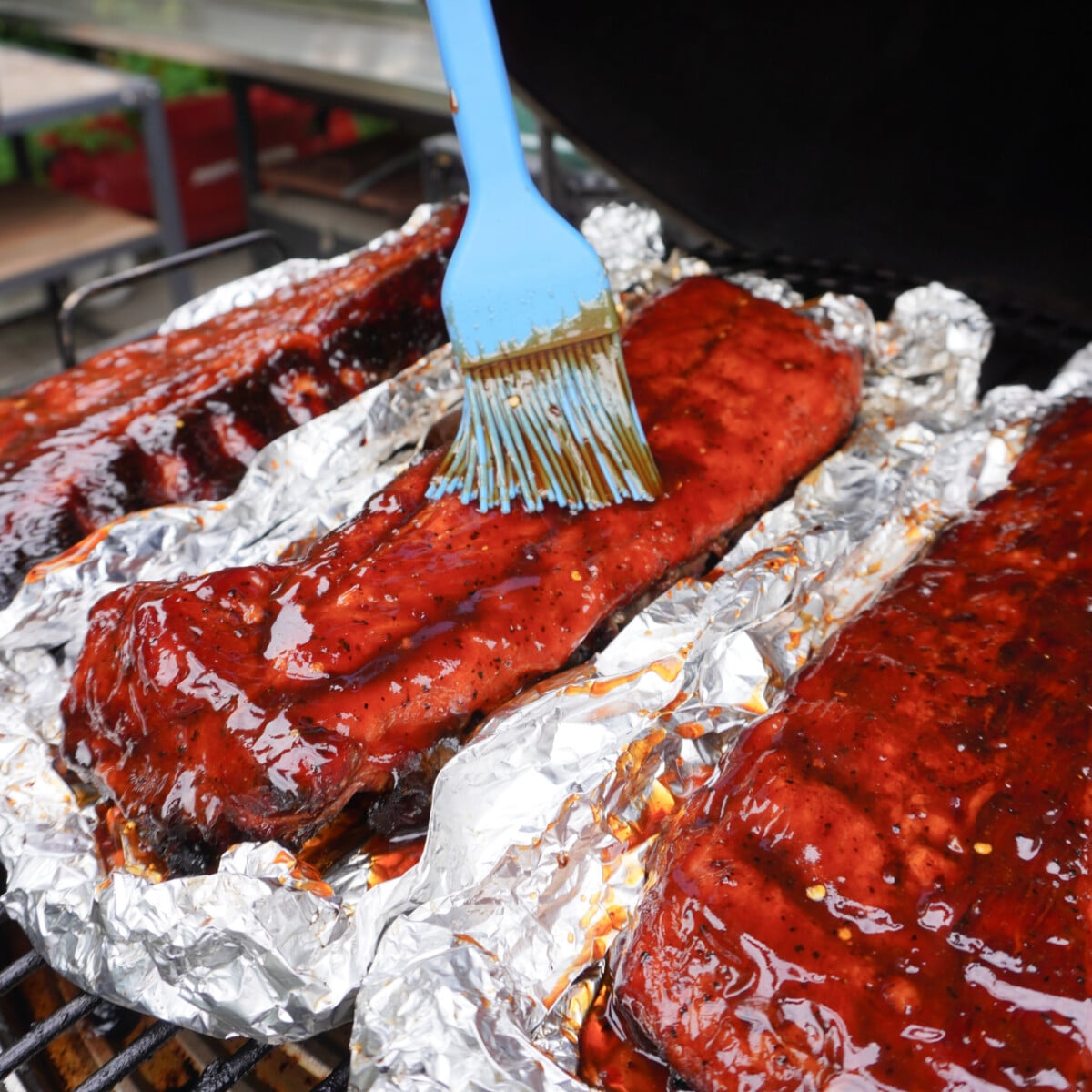 saucing up jack and coke smoked ribs in foil boats on the grill.