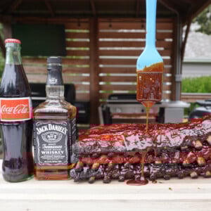 Jack and Coke Smoked Ribs with brush dripping sauce over the ribs and a bottle of coca cola and jack daniel's bottle.