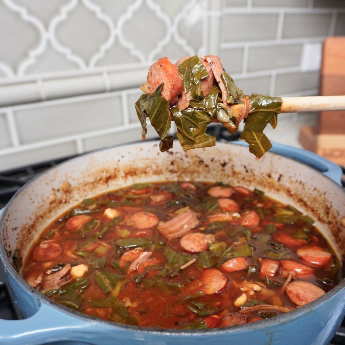 Collard Greens Cajun Gumbo scooped up on a wooden spoon over a pot.