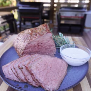 Smoked bottom round roast placed and sliced with a creamy garlic dipping sauce on the side.