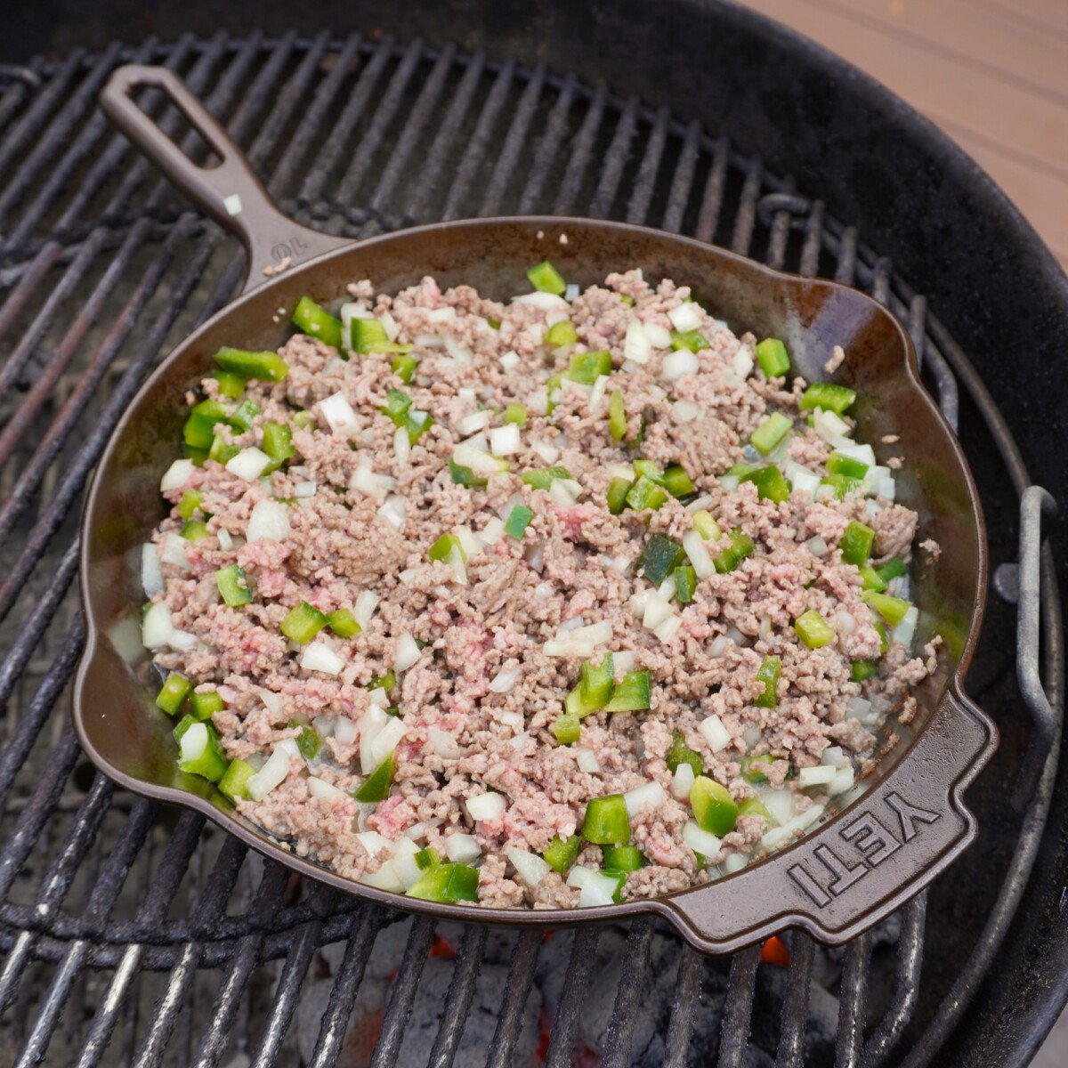 a cast iron skillet on the grill with cooked ground beef and chopped veggies.