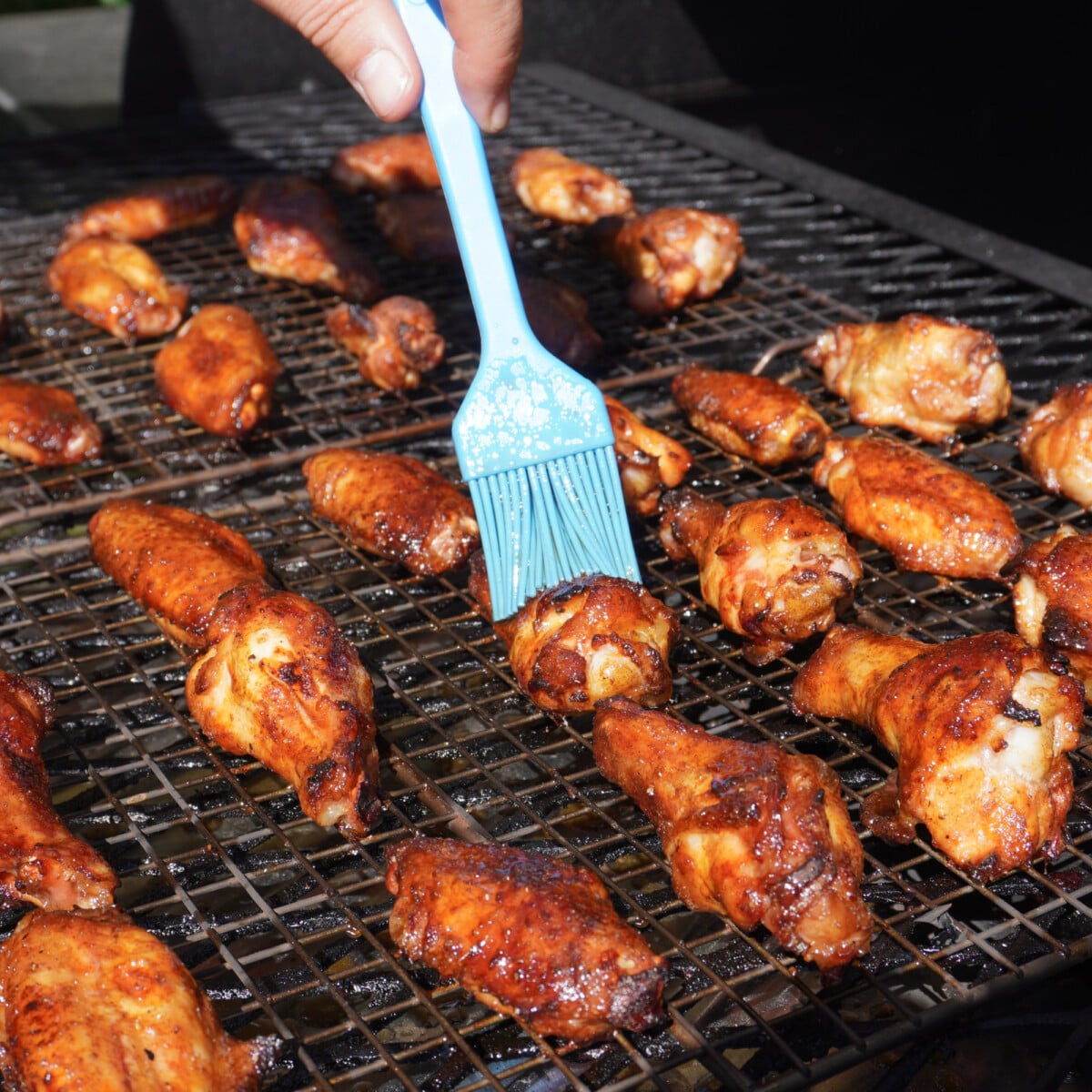brushing maple bourbon glaze over smoked chicken wings on the smoker.