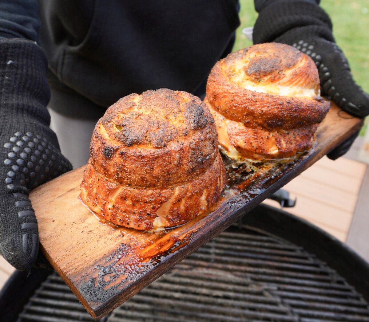 Grilled Jalapeno Popper Salmon Pinwheels on a cedar plank over a charcoal grill.
