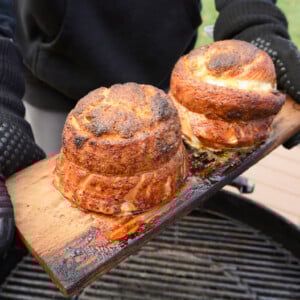 Grilled Jalapeno Popper Salmon Pinwheels on a cedar plank over a charcoal grill.