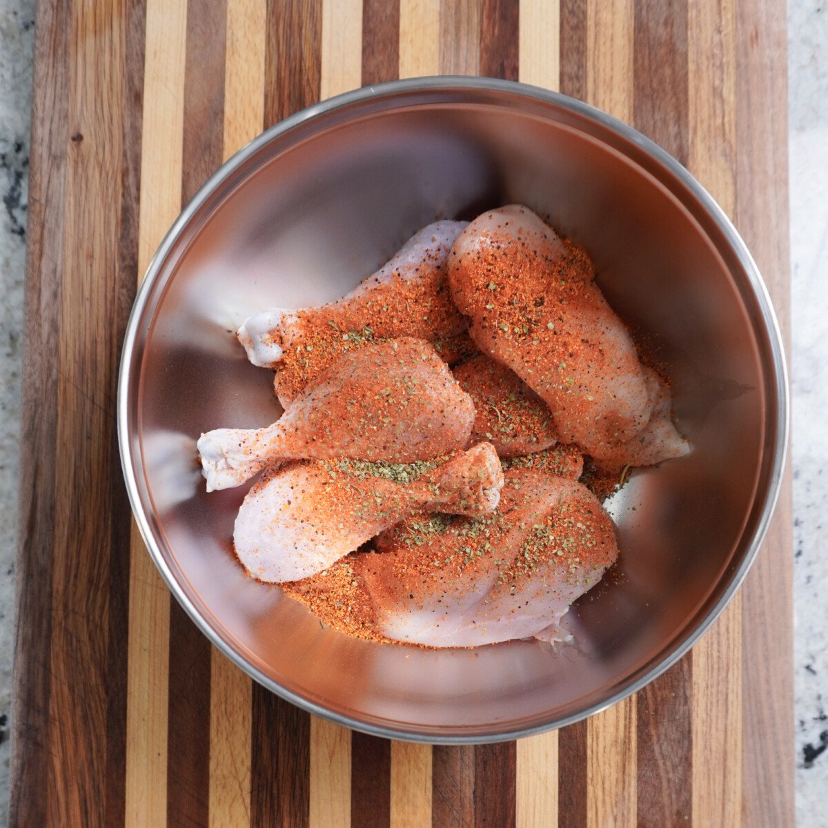 Raw chicken in bowl with seasonings.