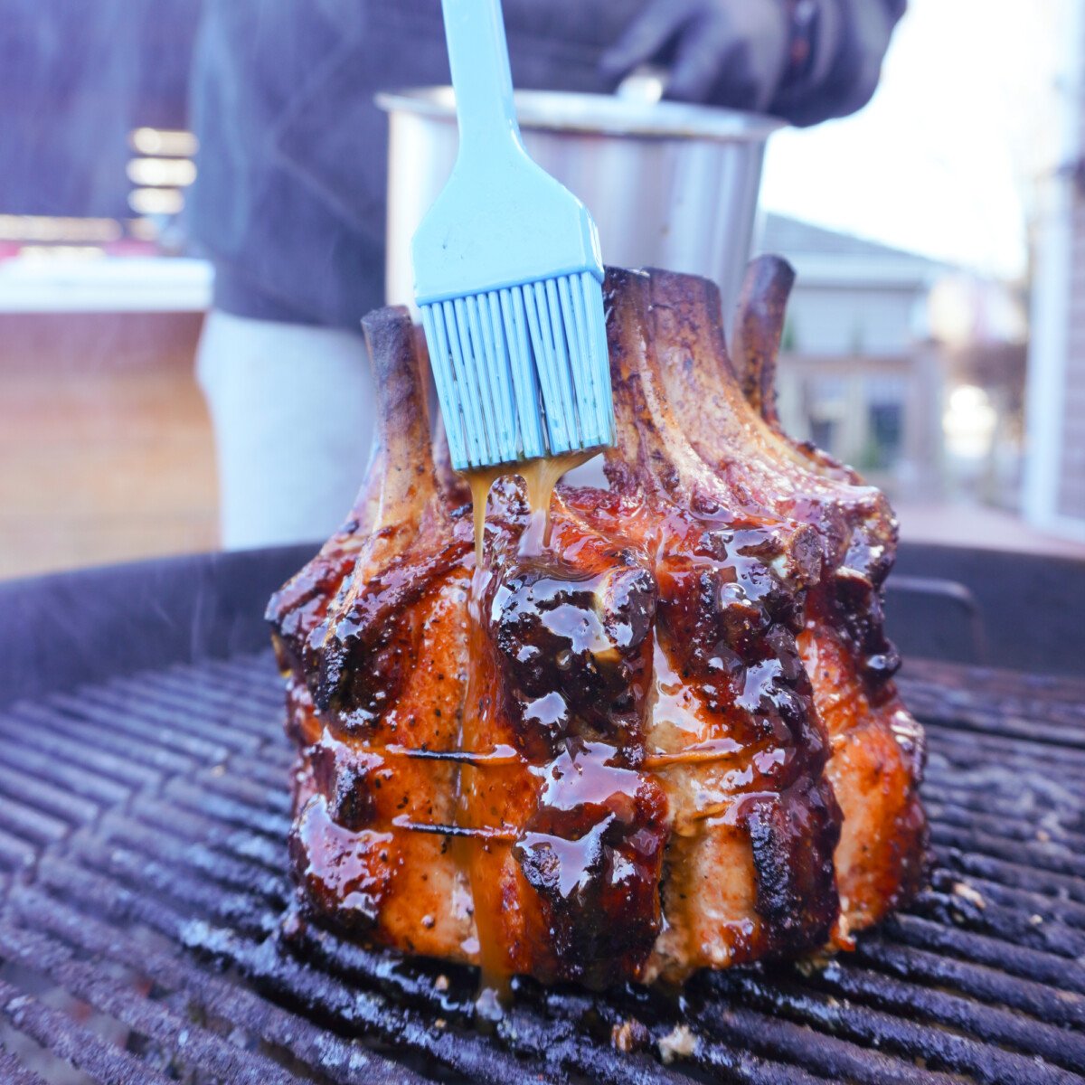 blue brush glazing a whiskey butter sauce over a grilled holiday crown roast.