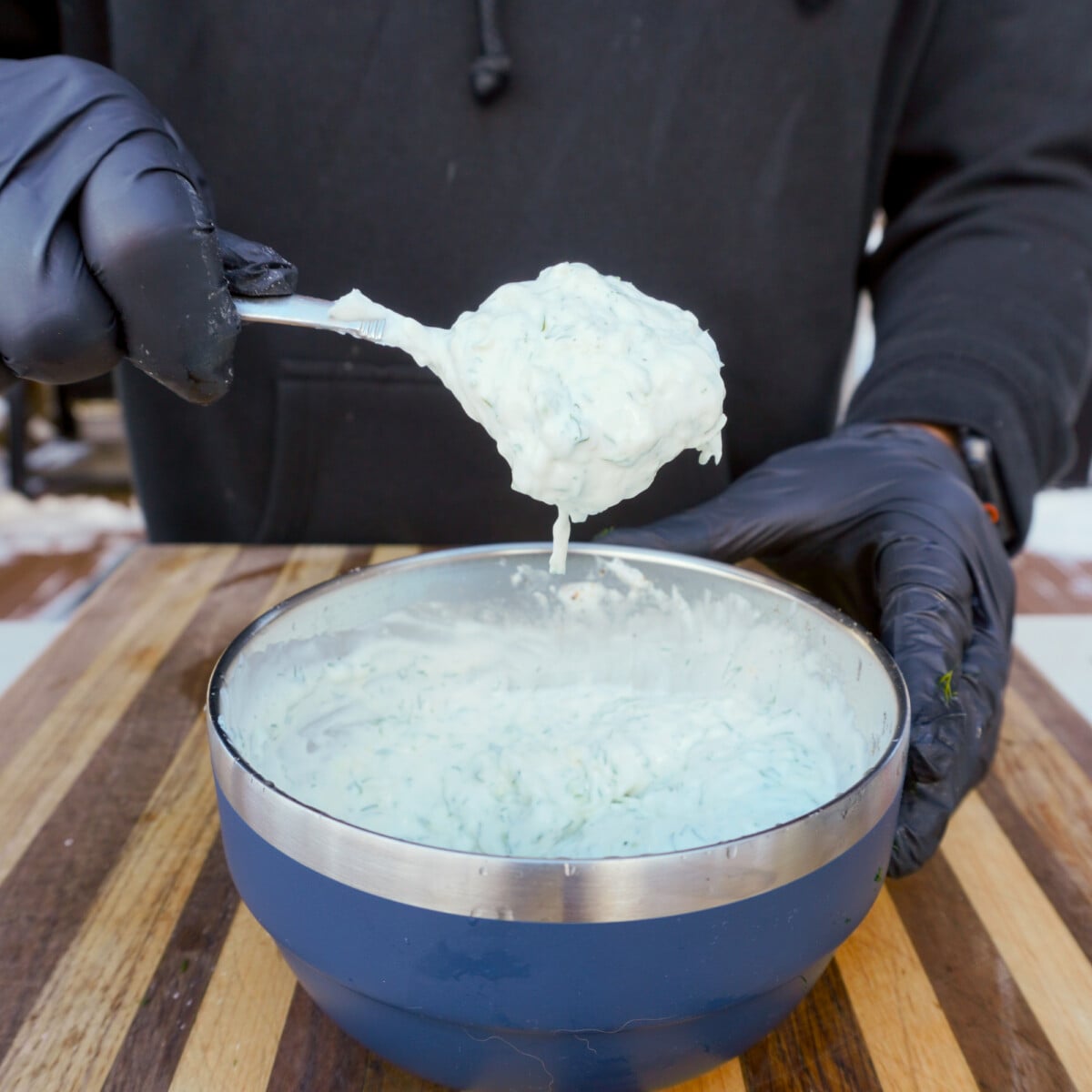 homemade tzatziki sauce in a spoon over a blue yeti serving bowl.