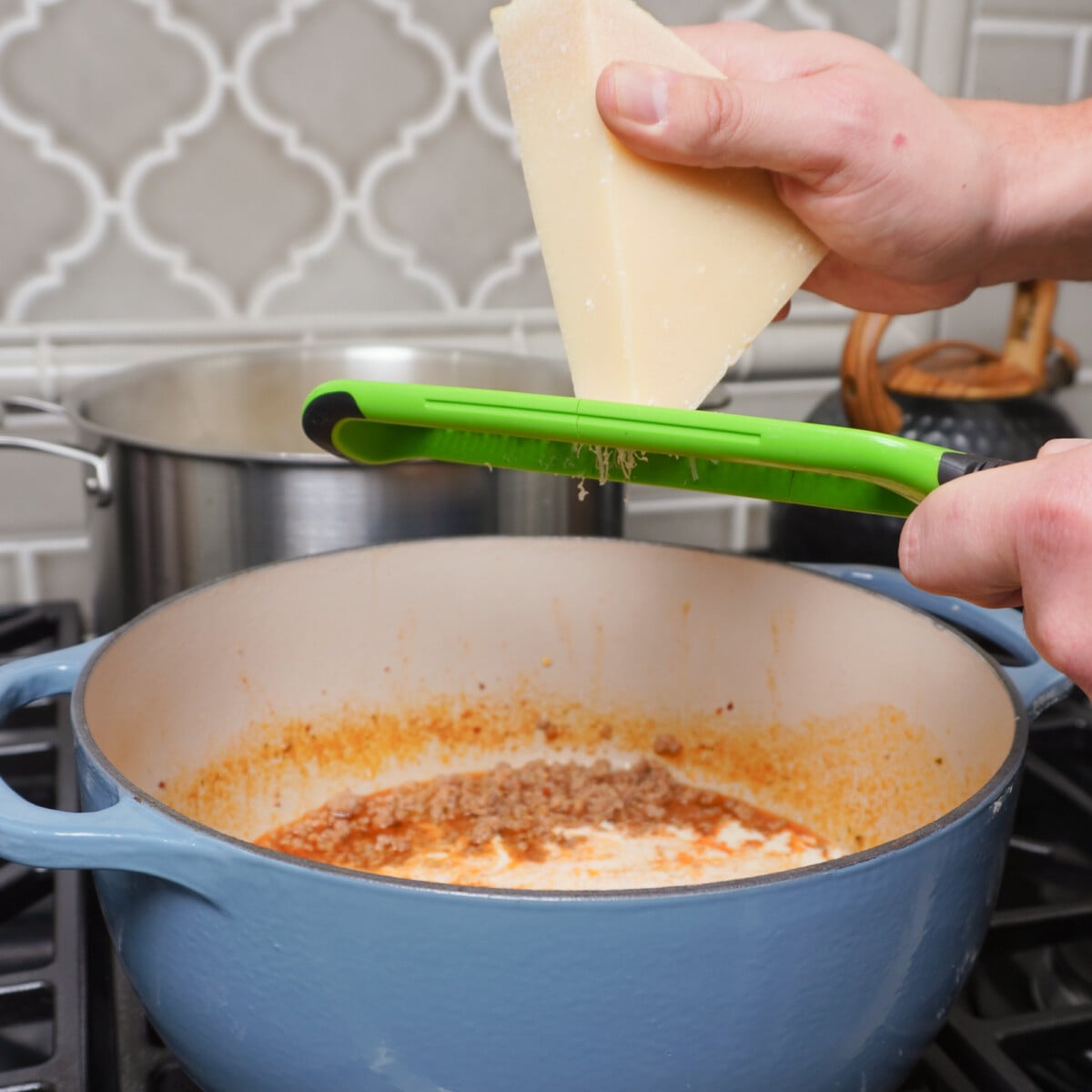 Grating a parmesan wedge over a pasta filled blue dutch oven.