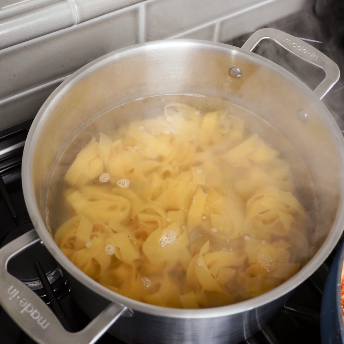 Pappardelle pasta cooking in pot.