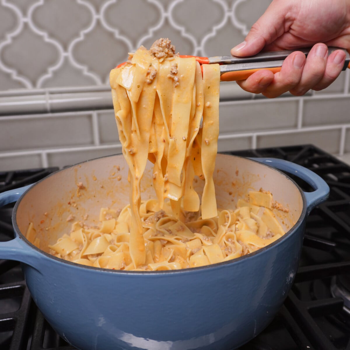 creamy Italian sausage pasta dish pulled out of dutch oven with tongs.