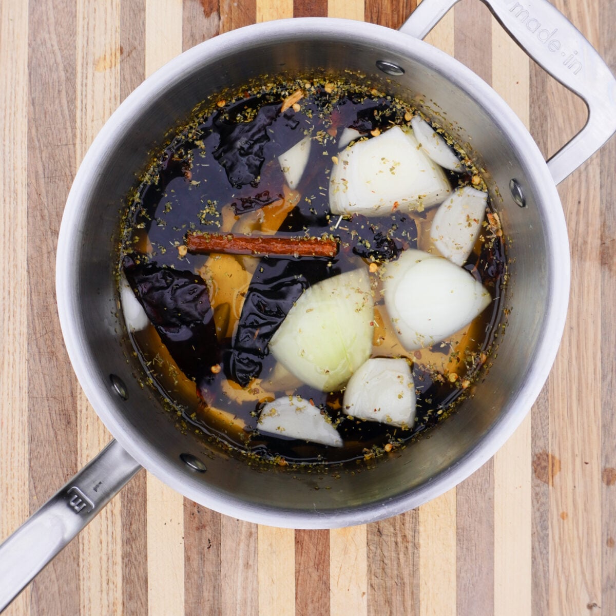 Adobo sauce liquid with chopped veggies and chilies in saucepan.