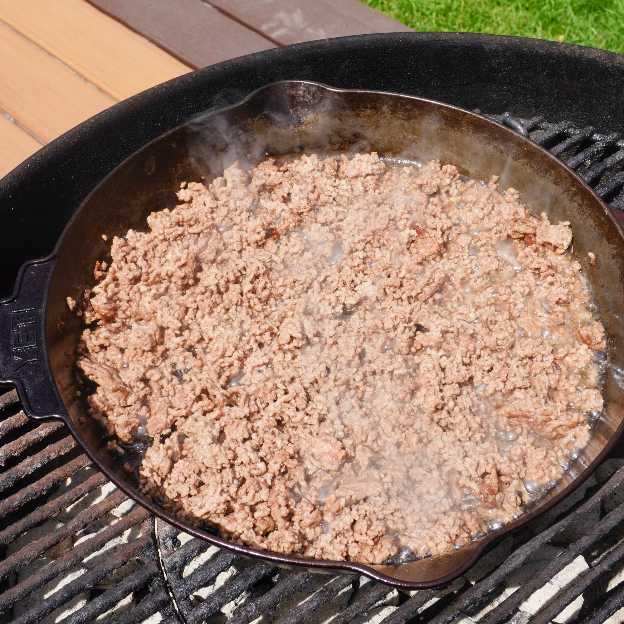 Ground beef in cast iron pan on a charcoal grill.