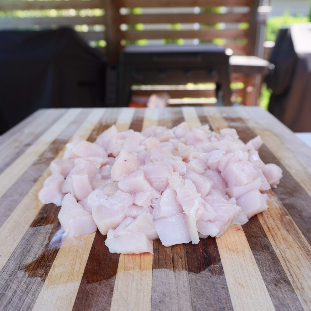 raw cubed chicken breast on wooden cutting board.