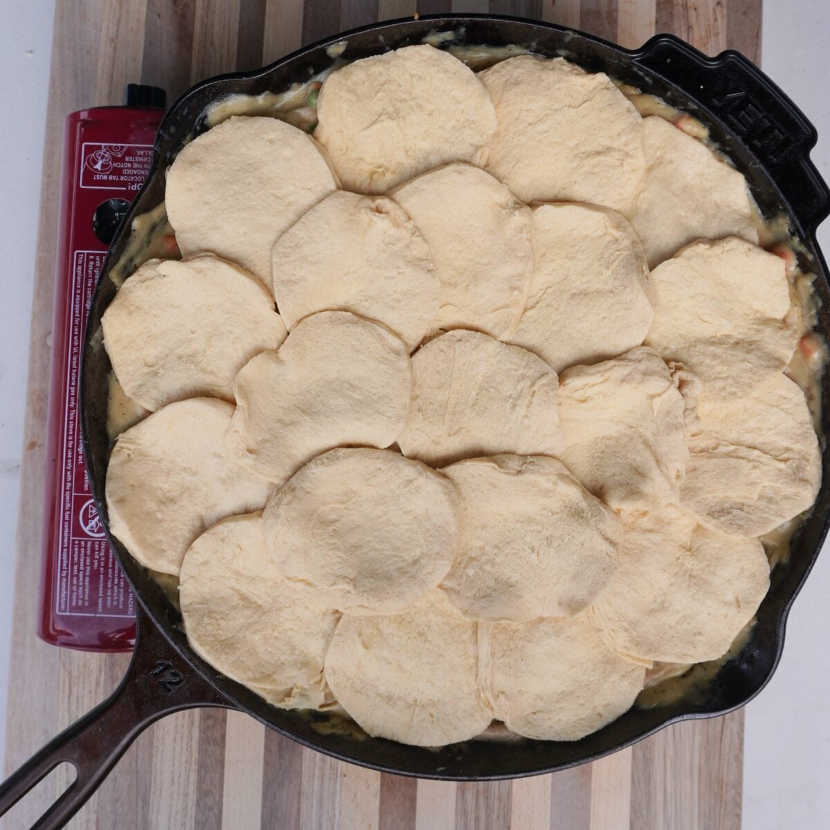 Layers of raw biscuit dough rounds over the smoked chicken pot pie filling in a cast iron skillet.