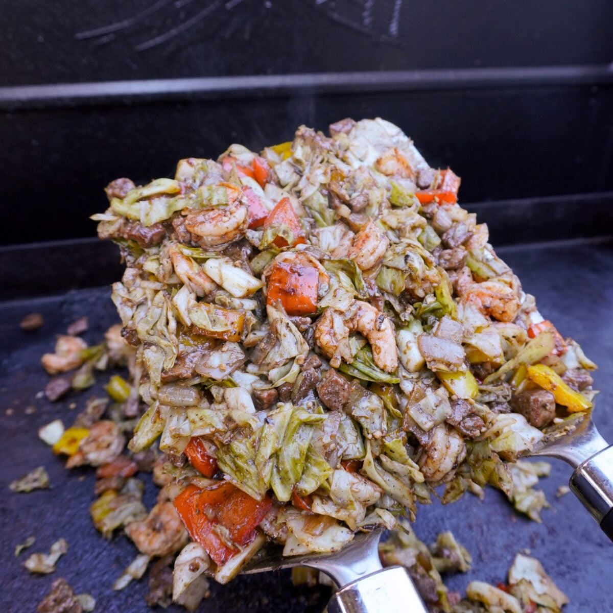 Surf and turf dirty cabbage scooped up on large griddle spatulas.